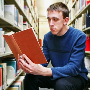 Kuva miehestä, joka lukee kirjastossa kirjaa.