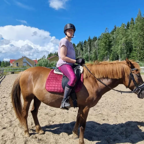 Nainen hevosen selässä ratsastuskentällä.