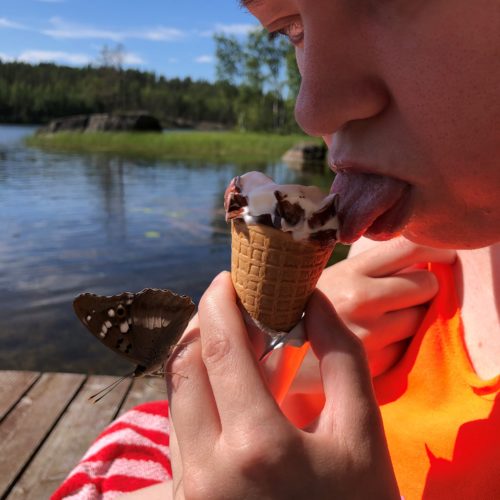 Tyttö syö jäätelöä. Tytön kädellä on perhonen.