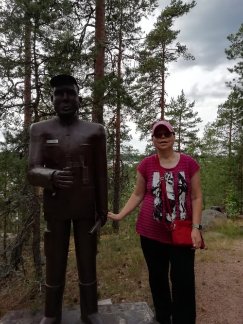Nainen seisoo metsässä patsaan vieressä.