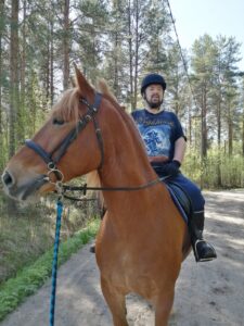 Mies istuu hevosen selässä maastossa