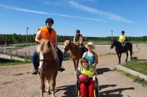 Ihmisiä hevosten kanssa tallin pihalla.