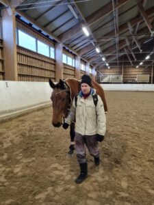 Mies taluttaa hevosta maneesissa.