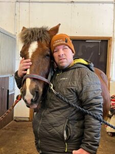 Mies nojaa päätään hevosen päätä vasten ja hymyilee.