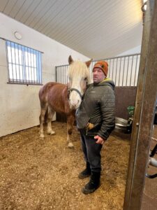 Mies ja hevonen seisovat vierekkäin pilttuussa ja katsovat kameraan.