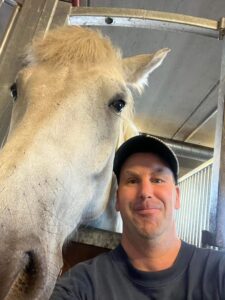 Valkoinen heppa ja mies katsovat kameraan.