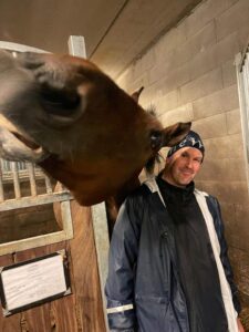 Hevonen ojentaa päätä kohti kameraa miehen olan yli.