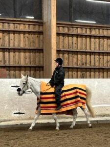 Mies ratsastaa hevoselle maneesissa. Hevosella on loimi selässä.