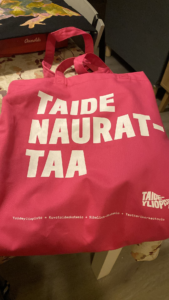 Pinkissä kangaskassissa lukee Taide naurattaa.